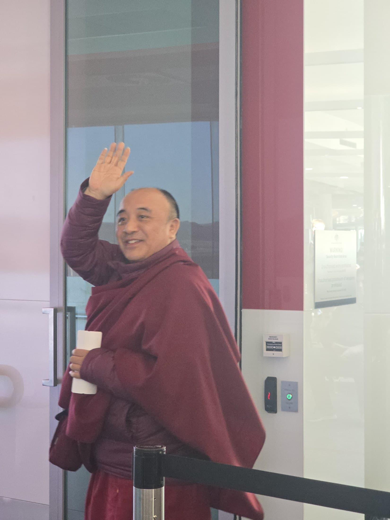 Kyabje Namkhai Nyingpo Rinpoche turning back with a smile and raised hand at the airport gate